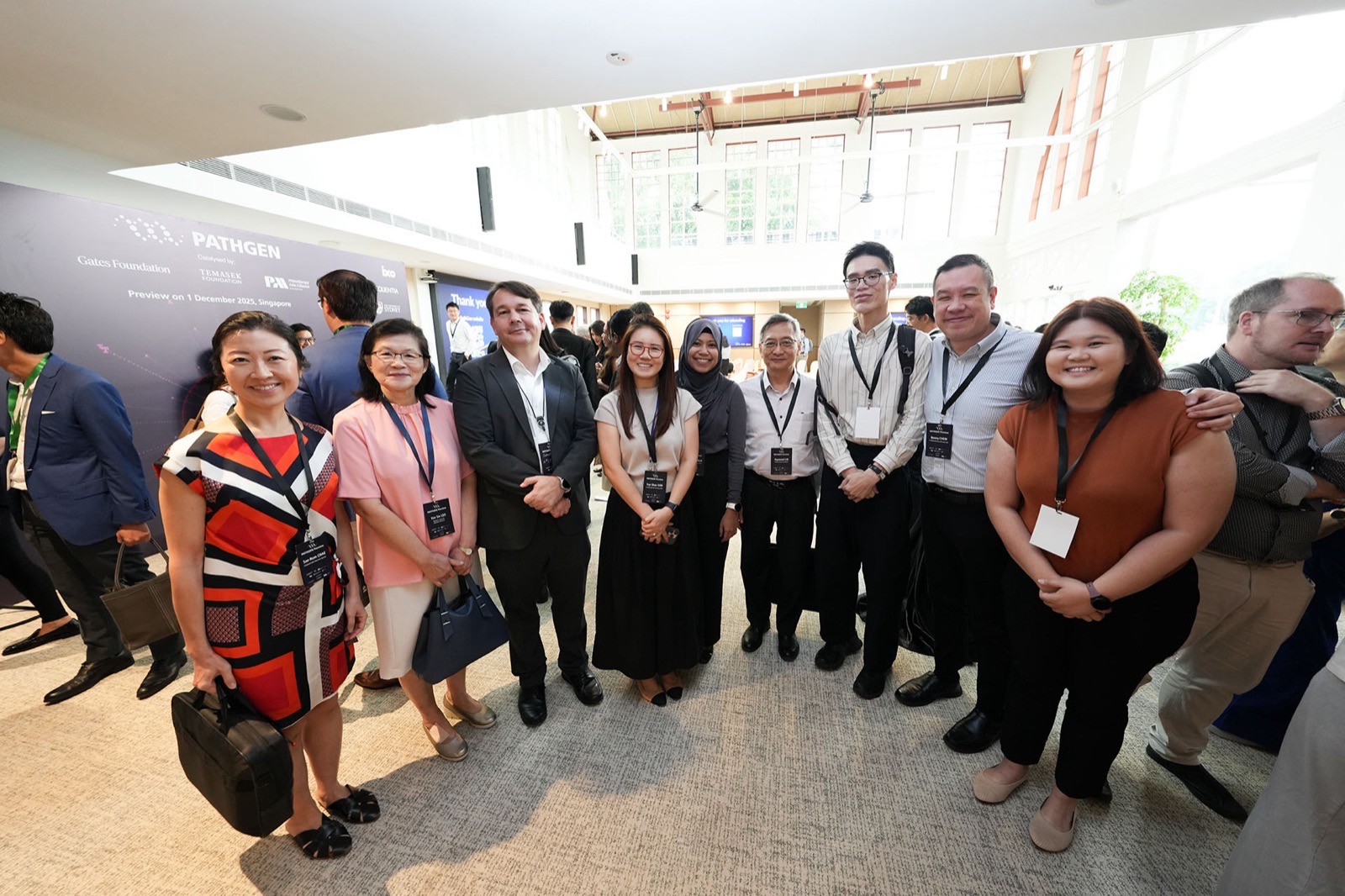 Guests wearing event lanyards standing together in the venue atrium in front of the PathGen preview backdrop.